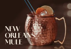 Ein glänzender Kupferbecher mit einem Cocktail, dekoriert mit Limettenscheiben und einer Orangenscheibe, auf einer dunklen Oberfläche.