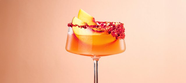 Fruchtige Peach Margarita mit ECKES Weißer Pfirsich Likör, Silver Tequila, Limettensaft und Crushed Ice, serviert in einer Cocktailschale mit Chili-Salzrand und garniert mit frischen Pfirsichscheiben.