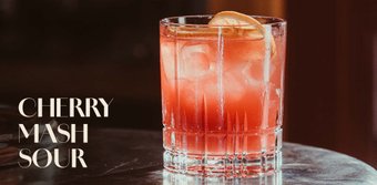 Der Cherry Mash Sour Cocktail, dekoriert mit einer Zitronenscheibe, steht auf einem eleganten Tisch aus Holz.