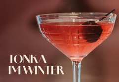 Das Glas mit dem Cocktail reflektiert das Licht, während die Kirsche im Getränk für einen Hauch von Farbe sorgt.