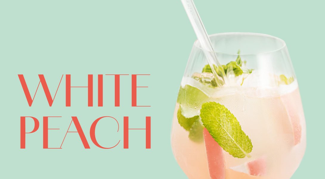 Glas mit hellrosa White Peach Cocktail, garniert mit Minzblättern und Eiswürfeln.
