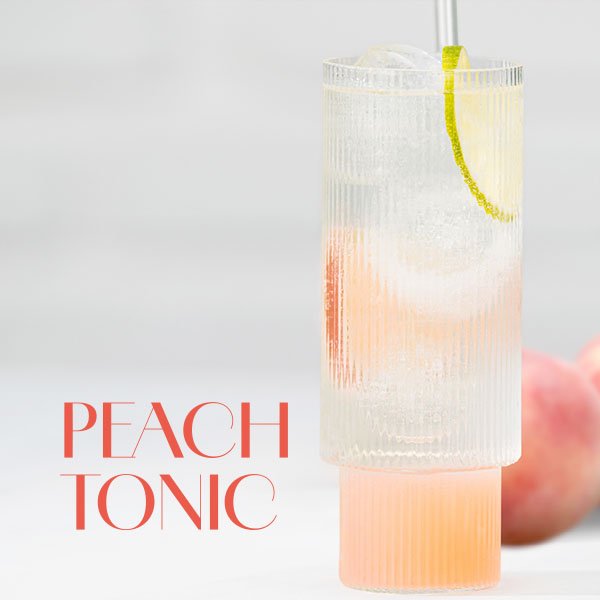 Hohes Glas mit hellrosa Peach Tonic Cocktail, garniert mit einer Limettenscheibe und Eiswürfeln.