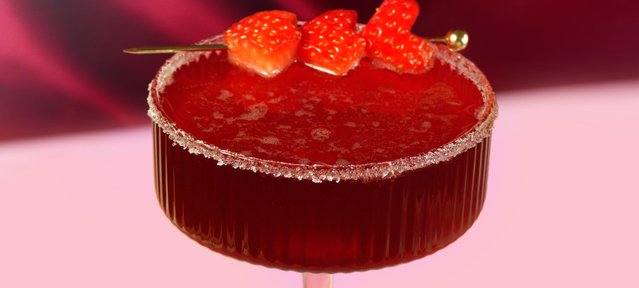 Ein elegantes Cocktailglas mit einem leuchtend roten Getränk, garniert mit frischen Erdbeeren auf einem goldenen Spieß.