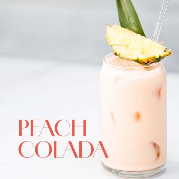 Glas mit rosa Peach Colada Cocktail, garniert mit einer Ananasscheibe und einem Ananasblatt.