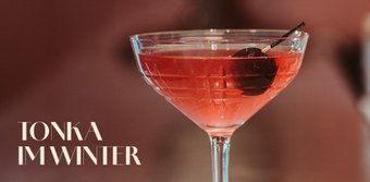 Das Glas mit dem Cocktail reflektiert das Licht, während die Kirsche im Getränk für einen Hauch von Farbe sorgt.