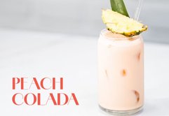 Ein köstlicher Peach Colada, serviert in einem Glas mit Eis, verziert mit einer frischen Ananasscheibe und einem Strohhalm.