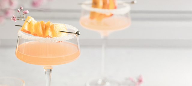 Zwei stilvolle Cocktails mit einem Hauch von Frucht und Zucker, die auf einem minimalistischen Tisch in sanften Farben präsentiert werden.