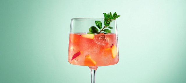 Erfrischender White Peach Cocktail mit ECKES Weißer Pfirsich Likör, Rosé Sekt und Bitter Lemon, garniert mit Minzblättern.