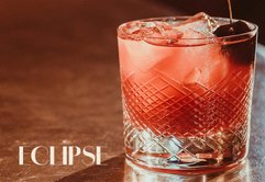 Der Cocktail im Glas hat eine leuchtend rote Farbe und wird von Eiswürfeln und einer Kirsche begleitet, ideal für einen Abend.