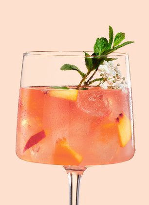Das Glas zeigt einen fruchtigen Cocktail, der mit Eis gefüllt ist und von einer grünen Minze und weißen Blüten geschmückt wird.