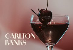Ein elegantes Cocktailglas mit dunkler Flüssigkeit und einer Kirsche, das auf einem stilvollen Tisch steht.
