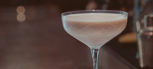 Glas mit ECKES Dirty Banana Cocktail, vor einem unscharfen Barhintergrund.