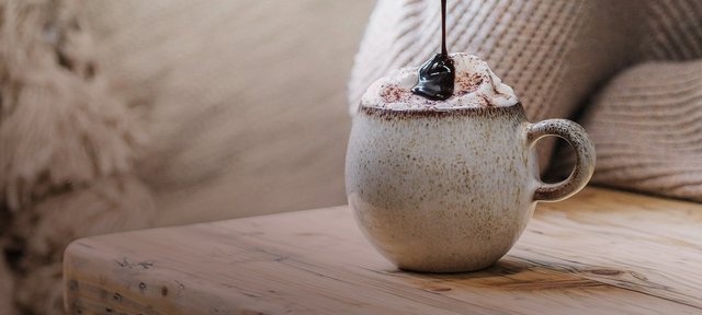 Tasse mit ECKES Chocolate Cherry, garniert mit Sahne und einer Kirsche, auf einem Holztisch vor einem gemütlichen Hintergrund.