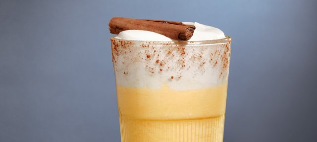 Glas mit ECKES Egg Nog Cocktail, garniert mit Zimtstange und Schokoladenstreuseln, vor einem grauen Hintergrund.
