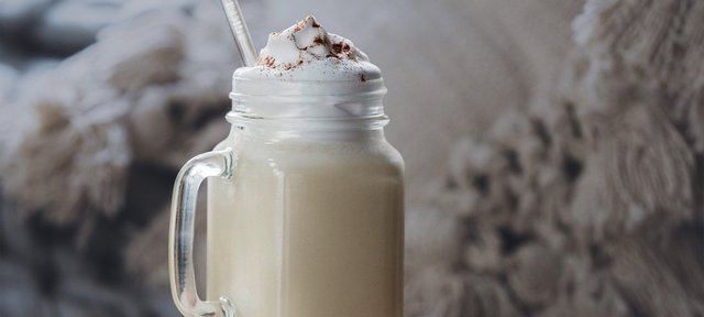 Glas mit ECKES Bombardino, garniert mit Sahne und Schokoladenstreuseln, vor einem unscharfen, gemütlichen Hintergrund.
