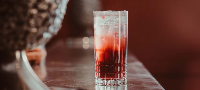 Glas mit einem ECKES Cherry Fizz Cocktail auf Eiswürfeln, auf einer Holzoberfläche vor einem unscharfen Hintergrund.